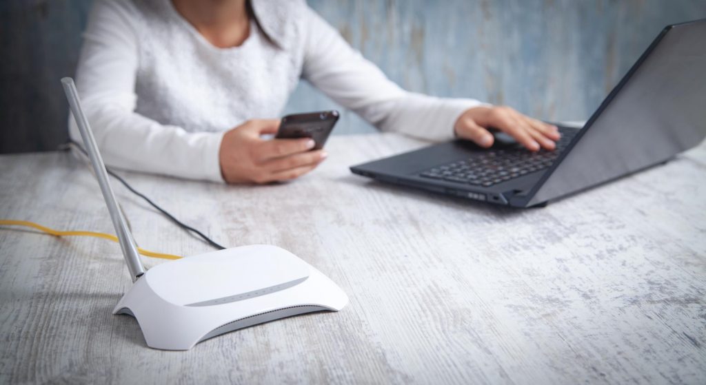 girl using smartphone and laptop in front of internet router